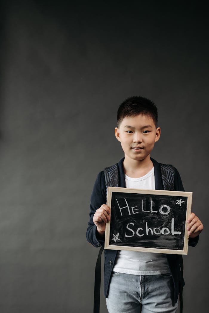 Portrait of a young boy holding a chalkboard with u0022Hello Schoolu0022 written on it, conveying excitement for school.